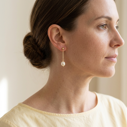 Model wearing pearl-style drop earring with pale yellow blouse