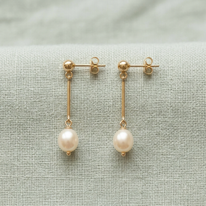 Pearl-style drop earring pair on pale sage linen